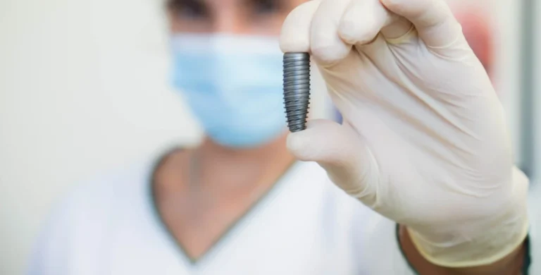 Dentista com farda dentária e máscara a segurar um implante